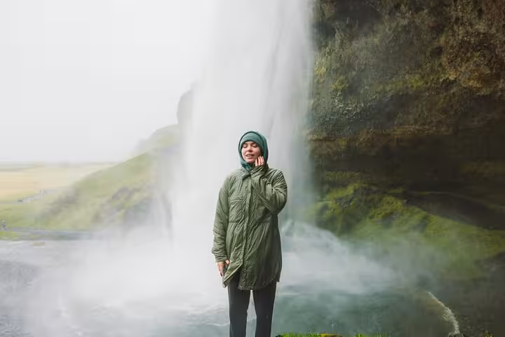 Woman in green jacket standing before misty Seljalandsfoss waterfall in South Iceland