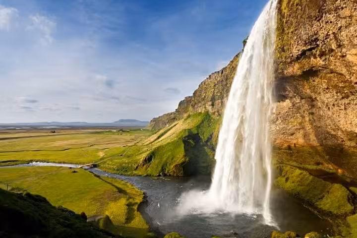 Majestic waterfall cascading over rocky cliffs into a river through green Iceland plains