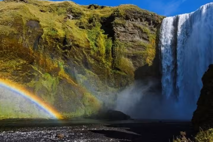 Skógafoss waterfall with rainbow mist over black sand beach in South Iceland