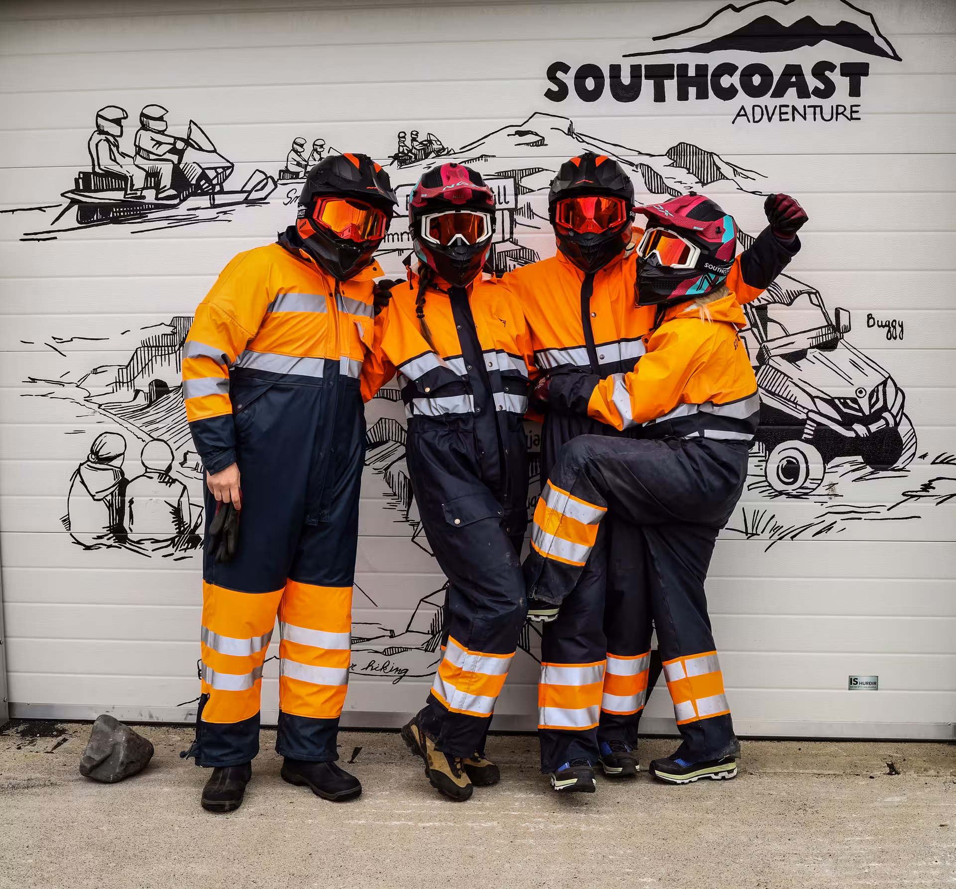 Four adventurers in orange safety suits and helmets posing at Southcoast Adventure buggy tour base in Iceland