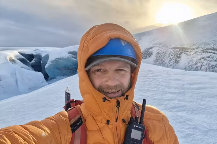 Guide in orange jacket and blue helmet takes selfie on glacier in Southeast Iceland