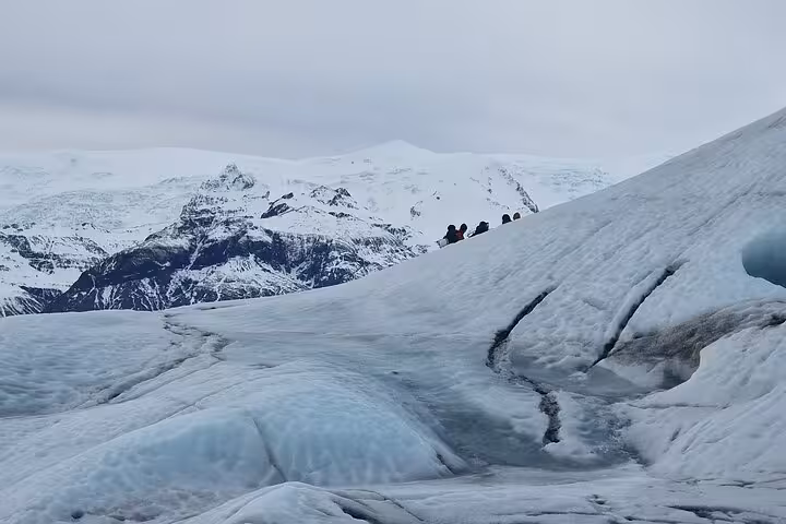 Hikers on a vast glacier with snow-capped mountains in southeast Iceland under overcast skies