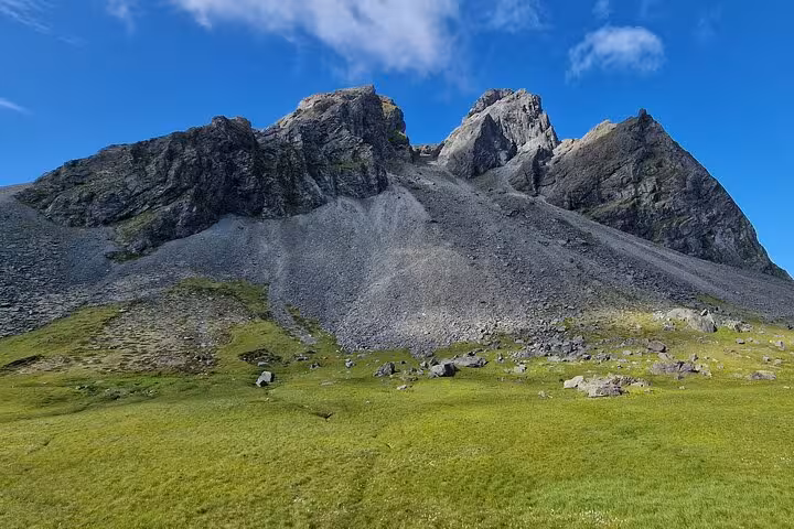 Rocky mountain peaks with scree slopes and green meadow in Southeast Iceland under blue sky
