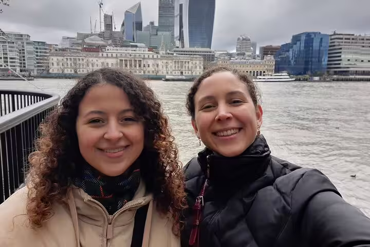 Two smiling women taking a selfie by the River Thames with London city skyline in background