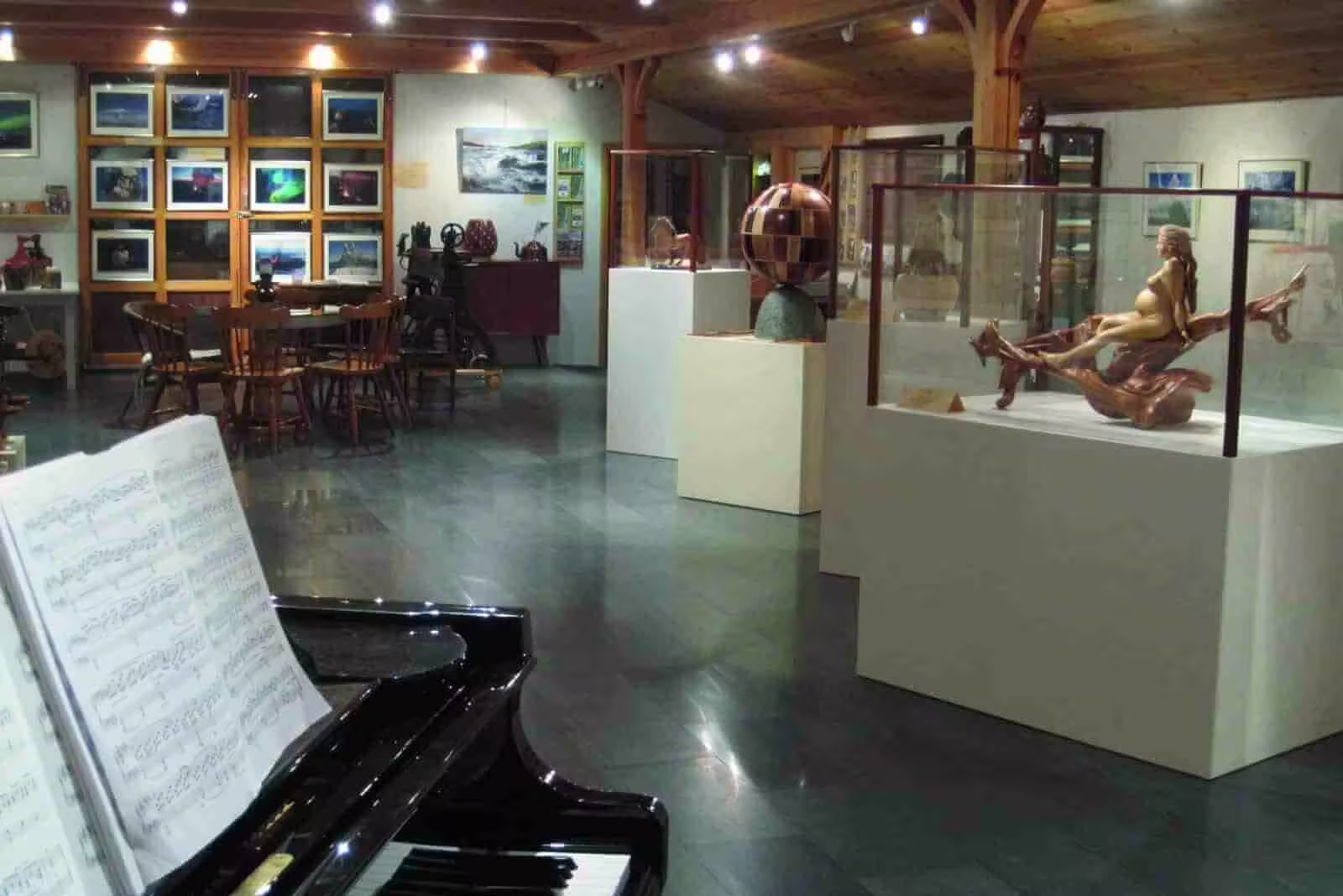Art gallery interior with grand piano, wood sculptures, and framed landscape paintings in Iceland