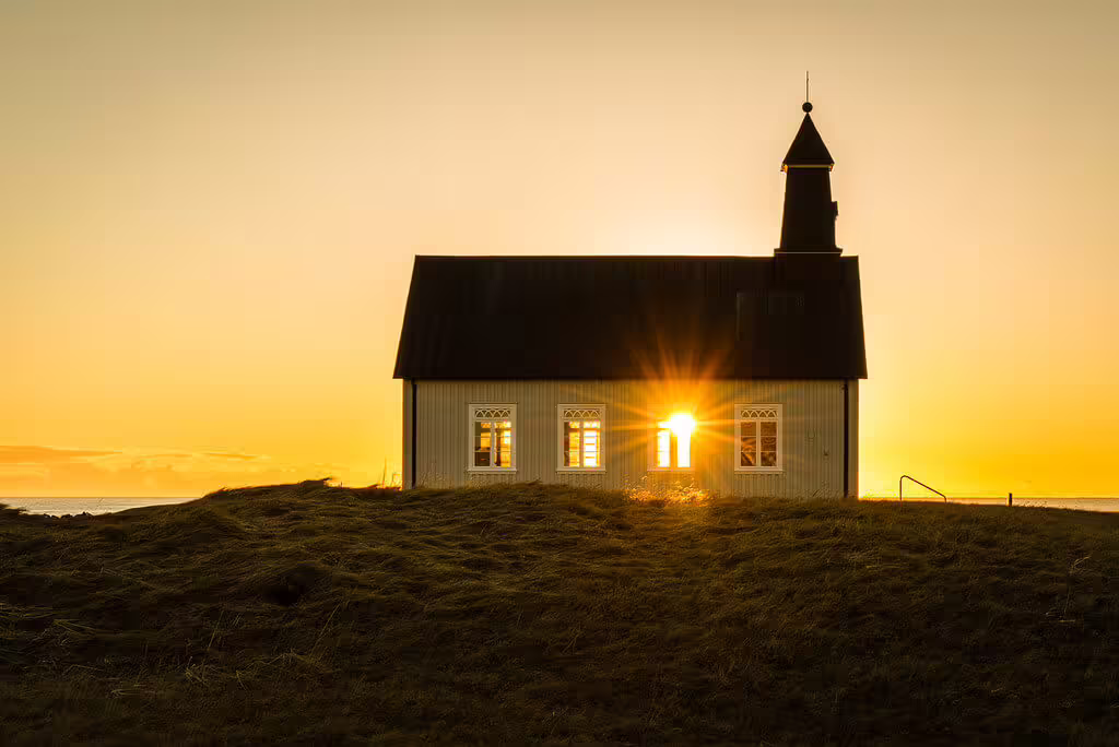 Small white church with black roof silhouetted against golden sunset in Southwest Iceland