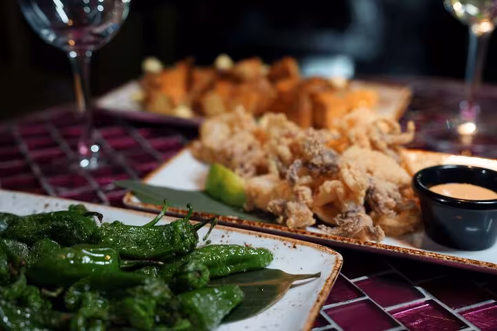 A variety of Spanish tapas including fried padrón peppers and calamari, showcasing a Barcelona culinary experience.