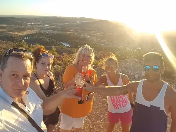Friends toasting glasses of sparkling wine at golden Algarve sunset viewpoint overlooking river valleys and rolling hills