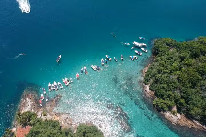 Drone shot of speedboats lined up along the sparkling turquoise waters and rocky coastline of Lagoa Azul.