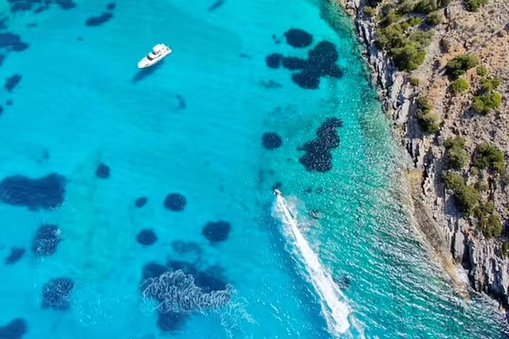 Aerial view of a speedboat cruising through crystal-clear blue waters near a rocky coastline.