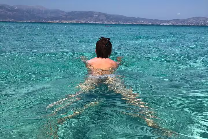 Person swimming in crystal-clear turquoise water with distant mountains, enjoying a refreshing break on a speedboat tour.