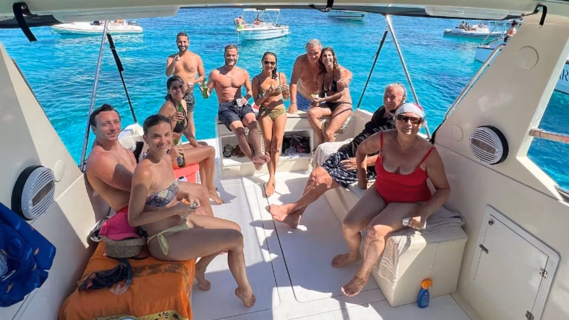 Group enjoying a lively boat tour in La Maddalena Archipelago, with turquoise sea and other boats in the background.