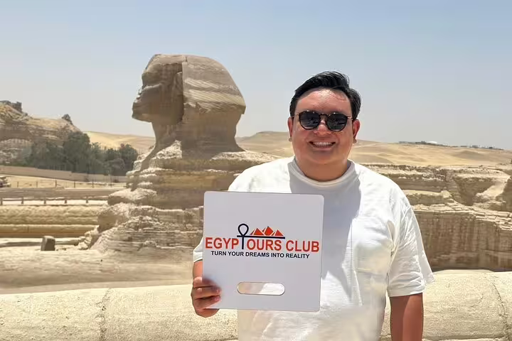 Traveler holding Egypt Tours Club sign with the Great Sphinx of Giza behind on a half-day pyramids tour