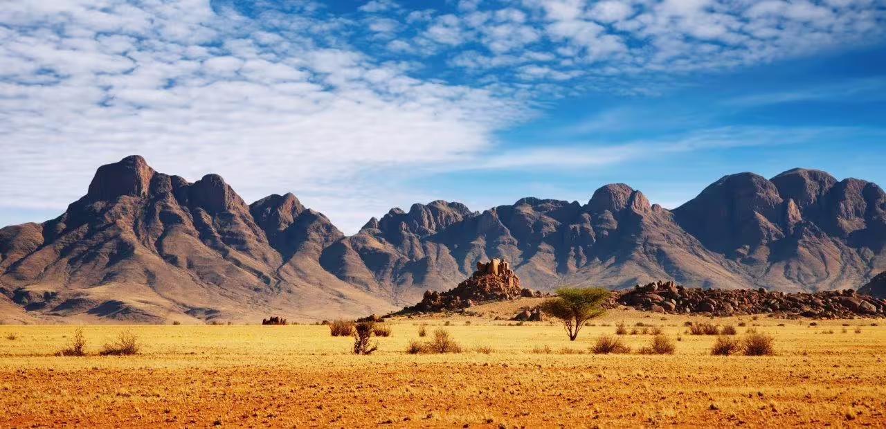 Majestic Spitzkoppe mountains rise against a vibrant sky in Namibia's sprawling desert landscape.
