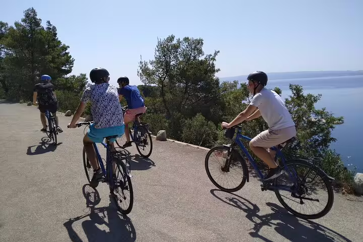 Cyclists on Split City Bike Tour riding a coastal road with sea views, helmets on, sunny Dalmatia