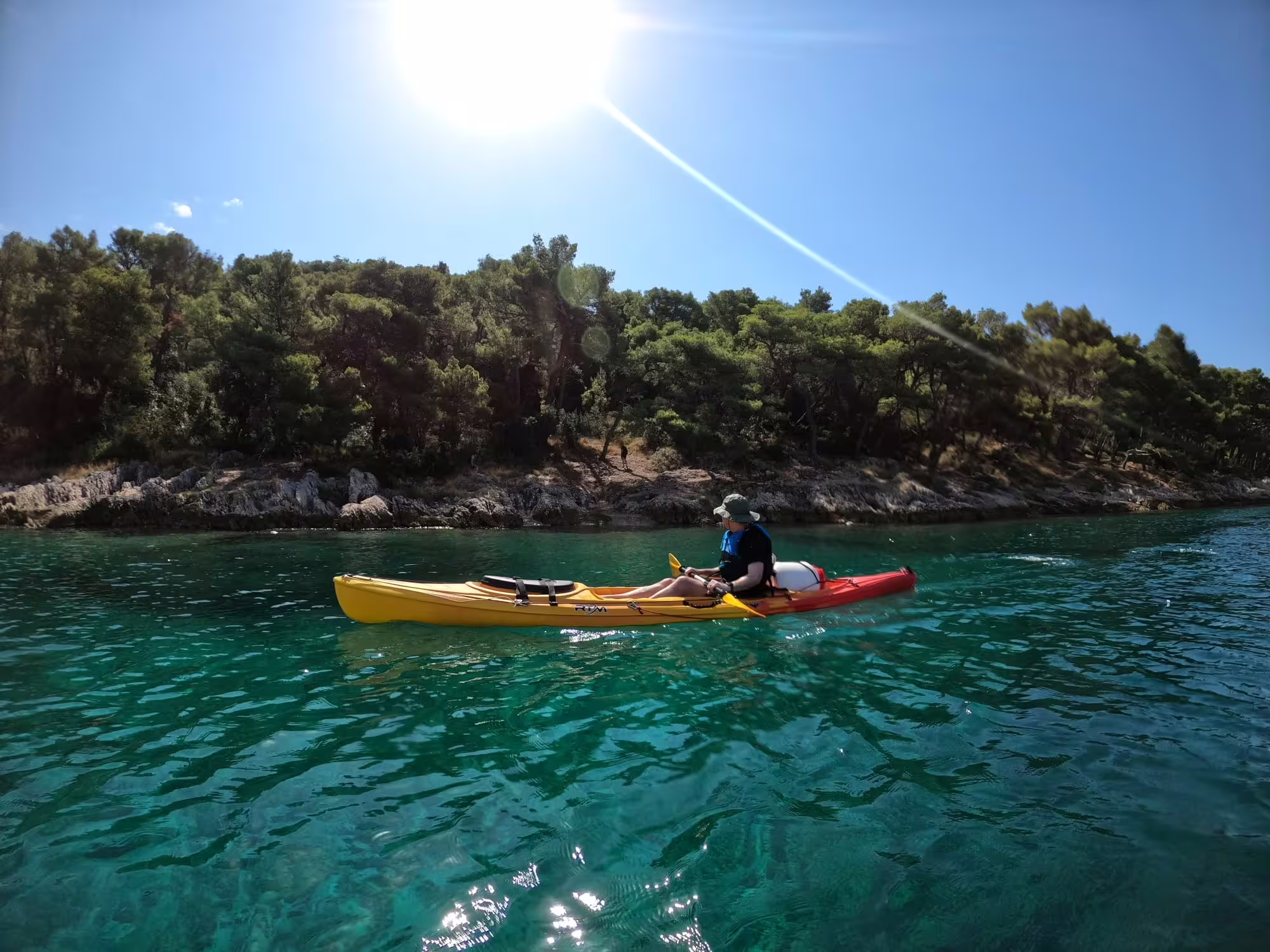 Kayaker paddling turquoise Adriatic near pine-lined coast on Split sea kayaking and snorkeling tour