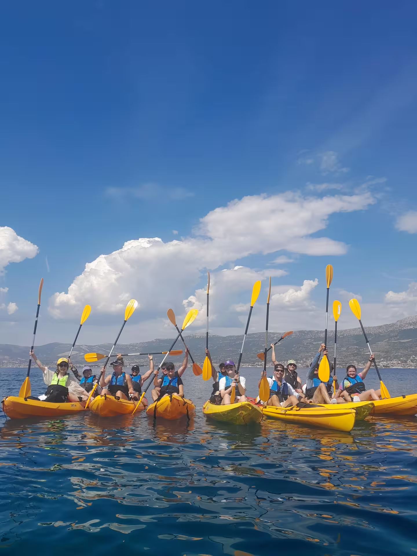 Happy group in yellow kayaks raising paddles on the Adriatic during a Split sea kayaking and snorkeling tour
