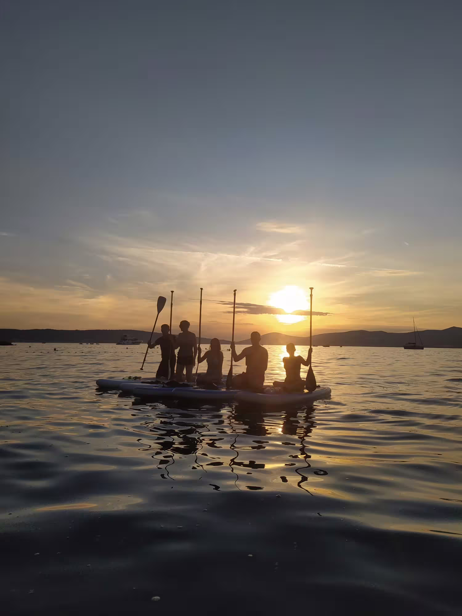 Split sunset SUP tour group resting on boards with paddles, Adriatic reflections and islands in the distance