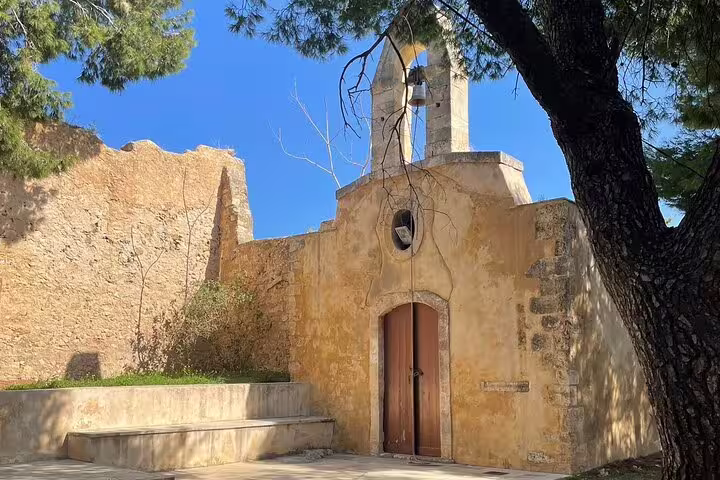 Charming St. Irini Monastery with rustic stone walls and bell tower, surrounded by lush greenery in Rethymno, Crete.