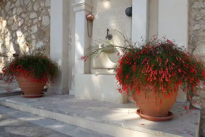 Charming stone fountain with vibrant red flowers at St. Irini Monastery, a serene stop on the Chania tour.