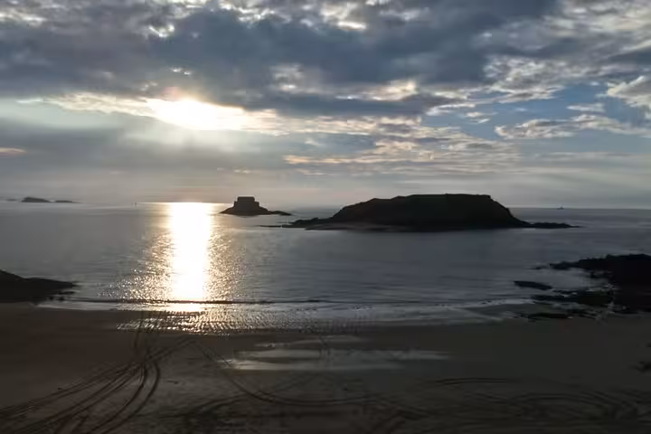 Sunset over St Malo bay with rocky islets and fort silhouette reflected on calm waters at low tide