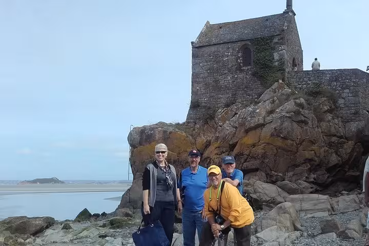 Tourists posing by a historic stone chapel on rocky Brittany coast during a private St Malo Dinan Cap Frehel day tour.
