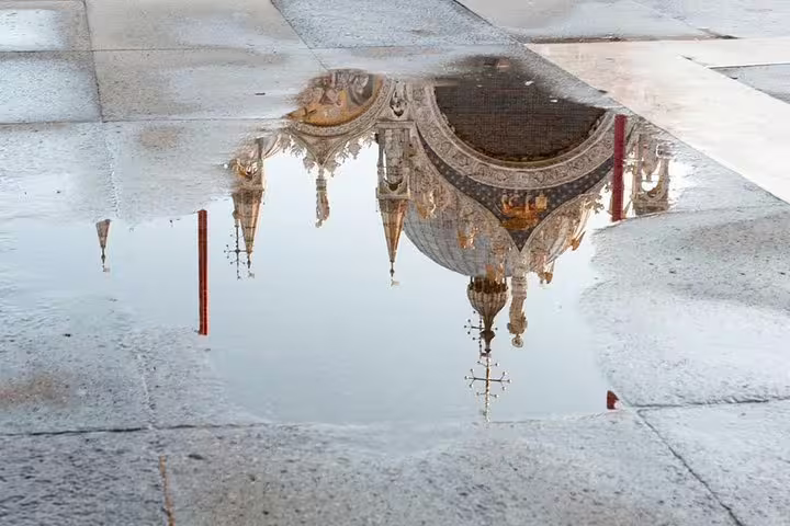 Reflection of St. Mark's Basilica's intricate domes in a rain puddle on the stone pavement in Venice, Italy.