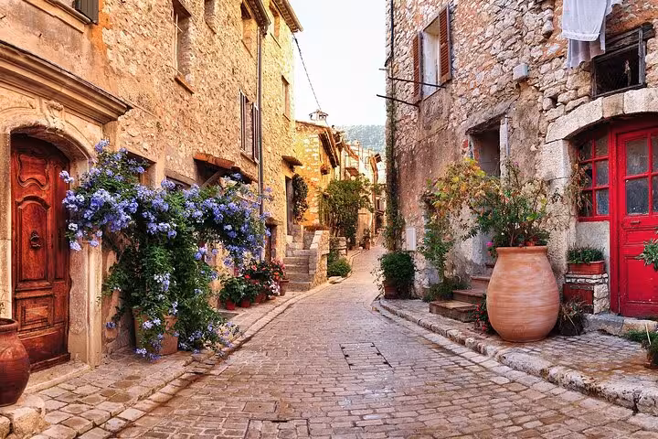 Charming cobblestone street in St Paul de Vence with stone buildings, red doors, and blooming blue flowers