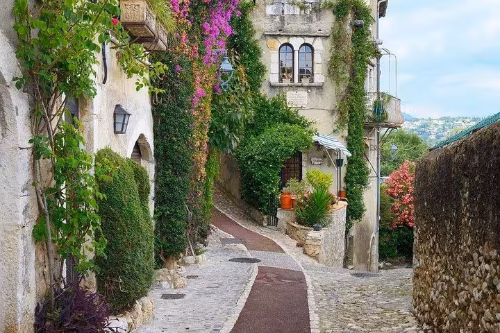 Narrow cobblestone alley in St Paul de Vence with ivy-covered stone walls and colorful bougainvillea flowers