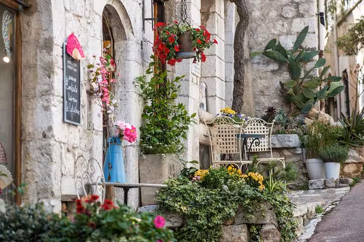 Charming stone street with colorful hanging flowers and white iron chairs in St-Paul-de-Vence, French Riviera