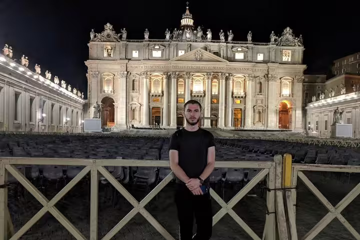 Man standing in front of illuminated St. Peter's Basilica at night in Vatican City, Rome