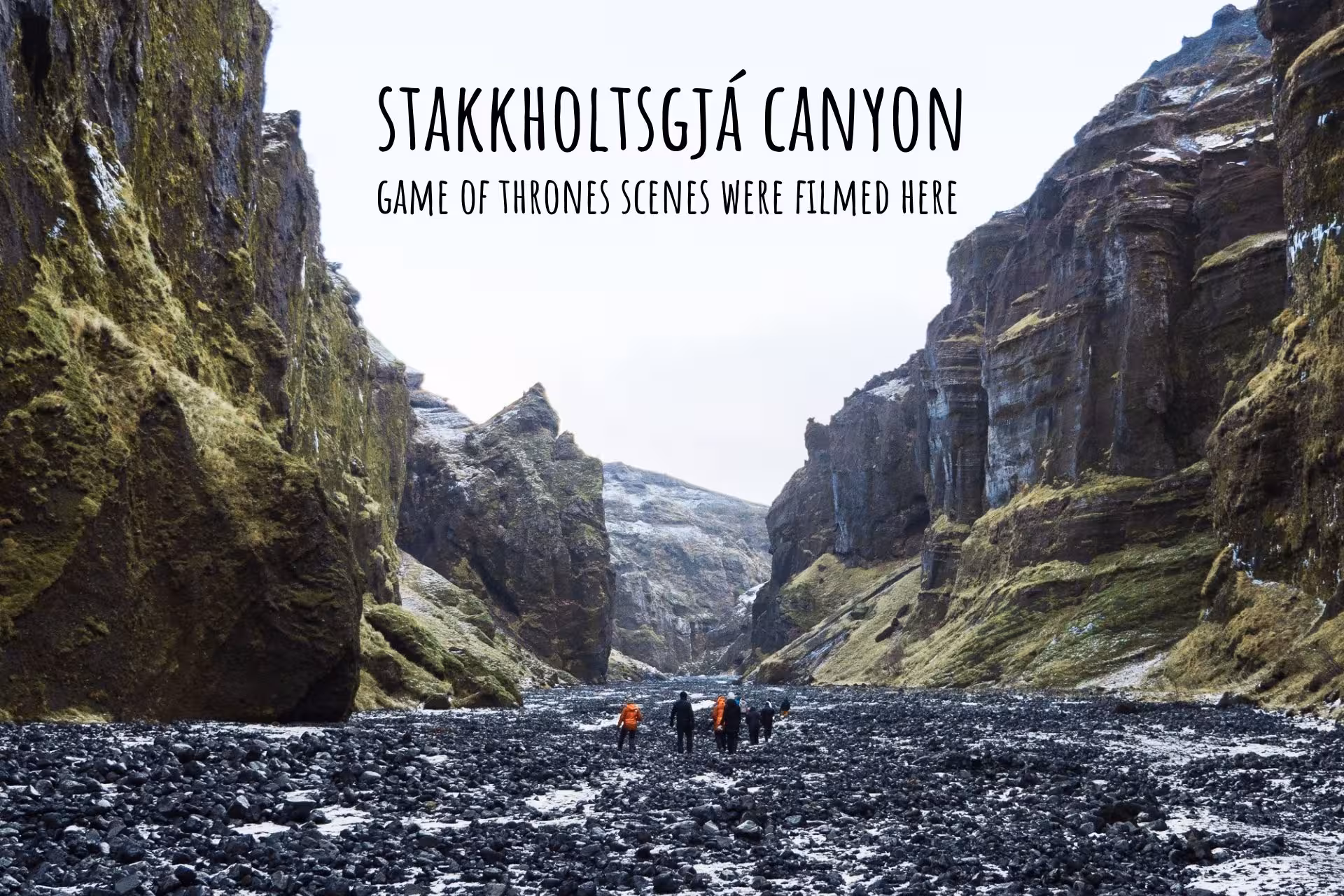 Hikers walking through Stakkholtsgjá Canyon in South Iceland, with towering moss-covered basalt walls