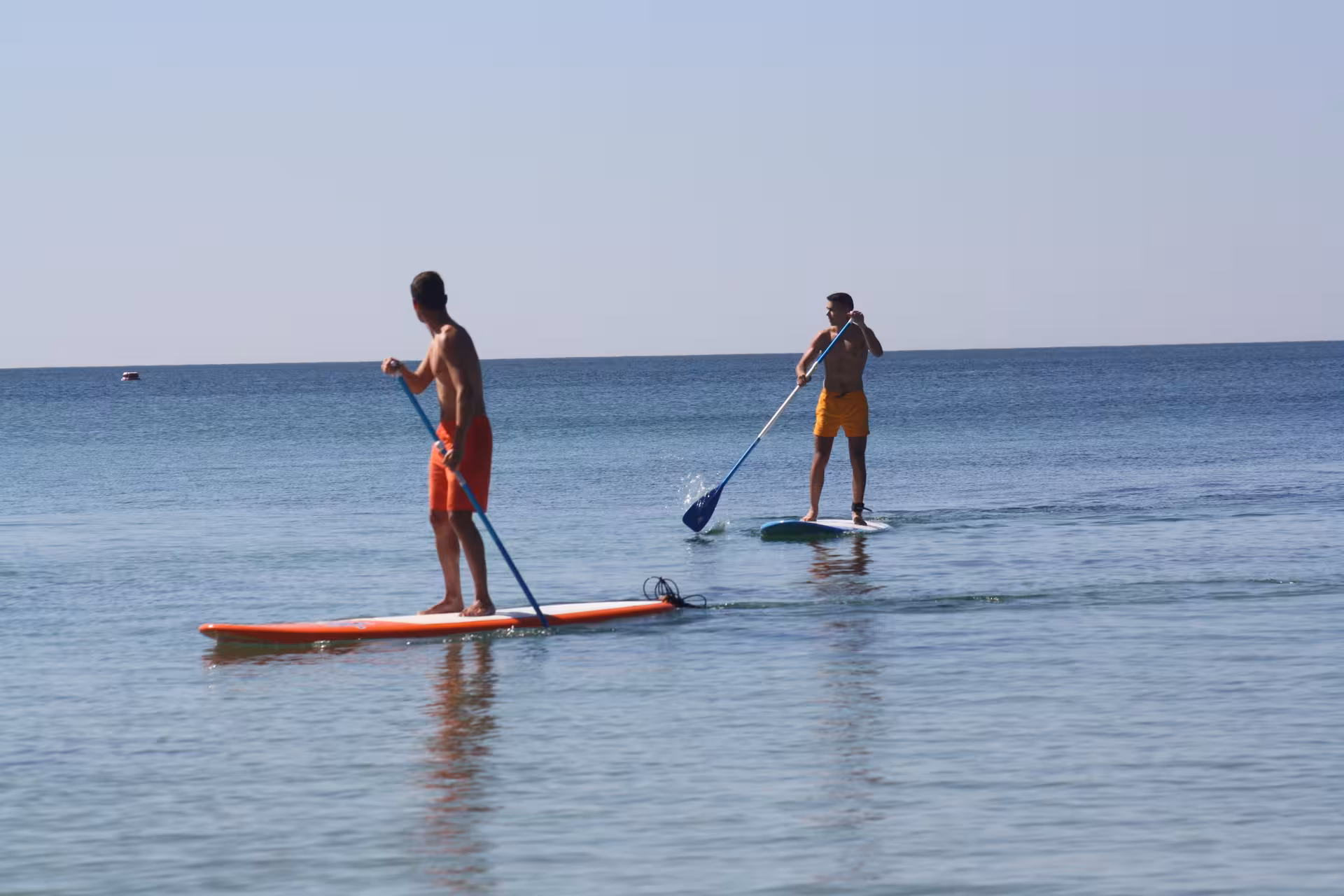 Two men enjoying stand up paddle board rentals side by side on a sunny clear blue sea
