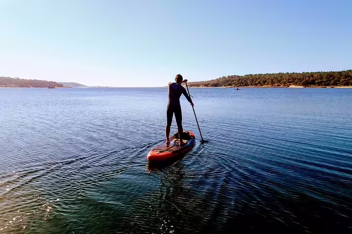 Person paddleboarding on calm waters with scenic views of Lisbon's coastline, perfect for a stand-up paddle adventure tour.