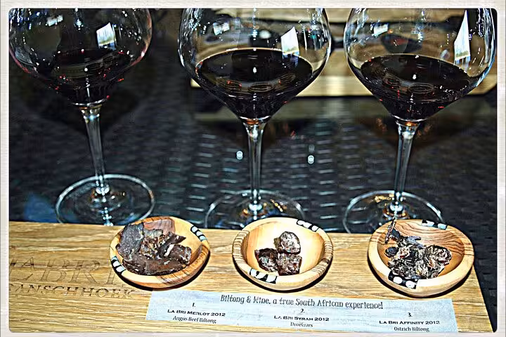 Three glasses of red wine paired with South African biltong samples, showcasing a Stellenbosch wine tasting experience.