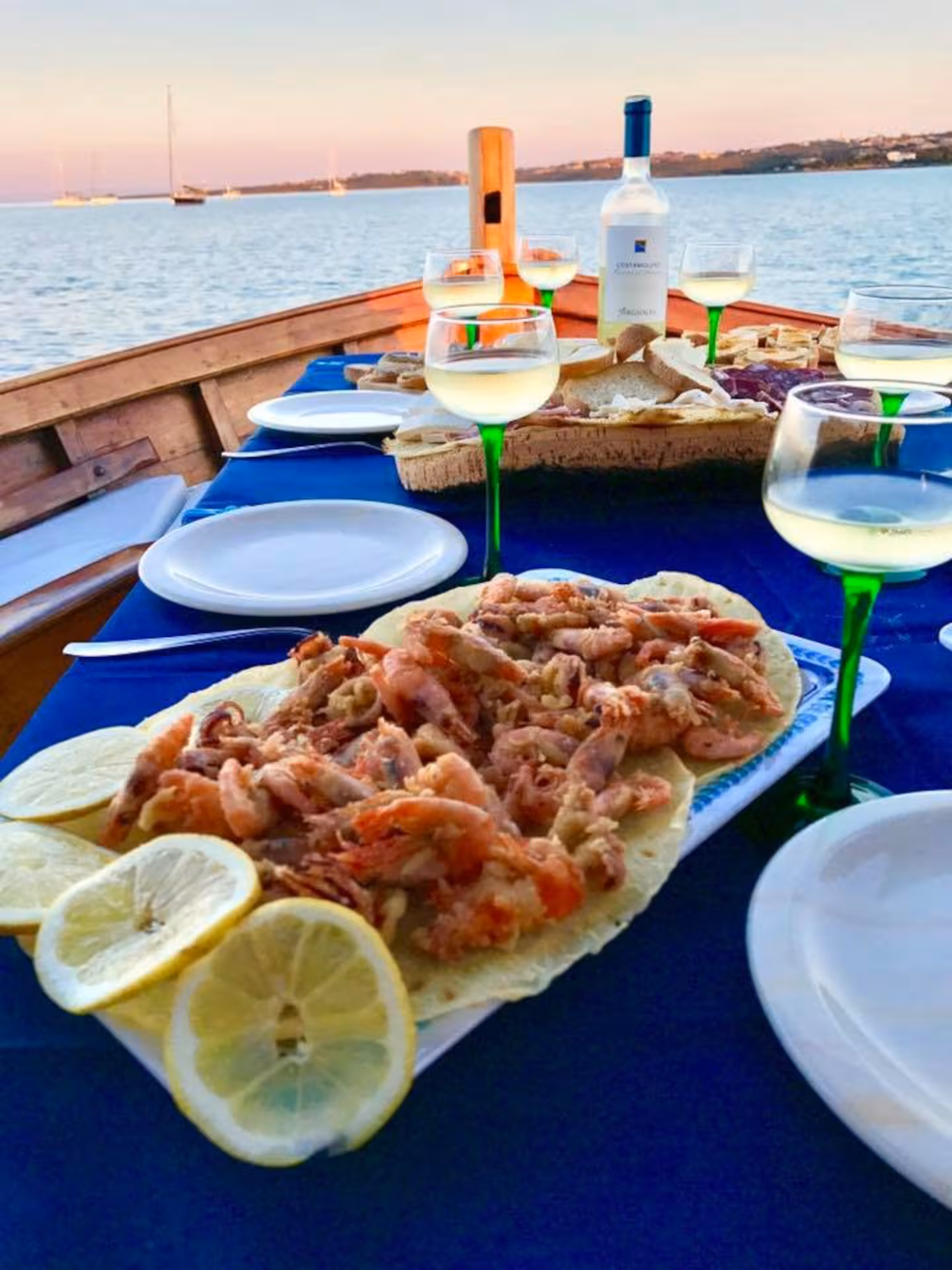 Dining setup with seafood and white wine on a boat during a sunset Asinara Island tour from Stintino.