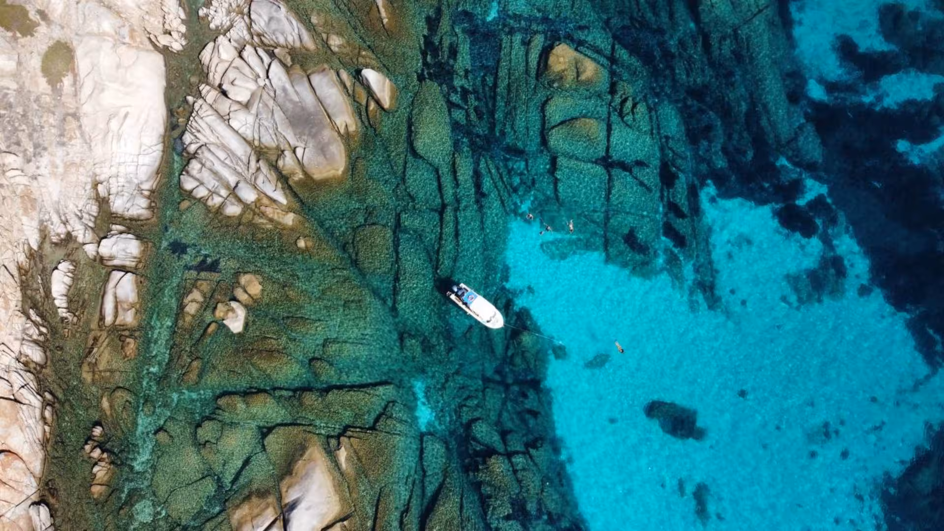 Aerial view of a boat in crystal-clear waters near rocky shoreline on Stintino to Asinara tour with aperitif.