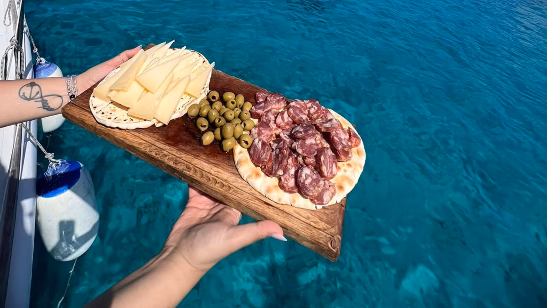 Delicious cheese, olives, and salami platter served on a wooden board against the backdrop of Asinara's blue sea.