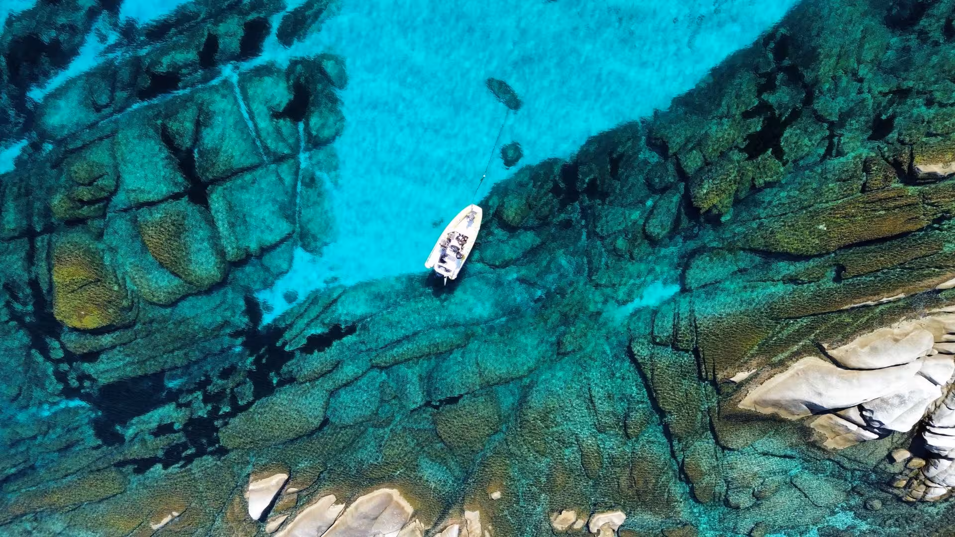 Aerial view of a dinghy anchored in turquoise waters, highlighting Asinara's vibrant marine life and rugged coastline.