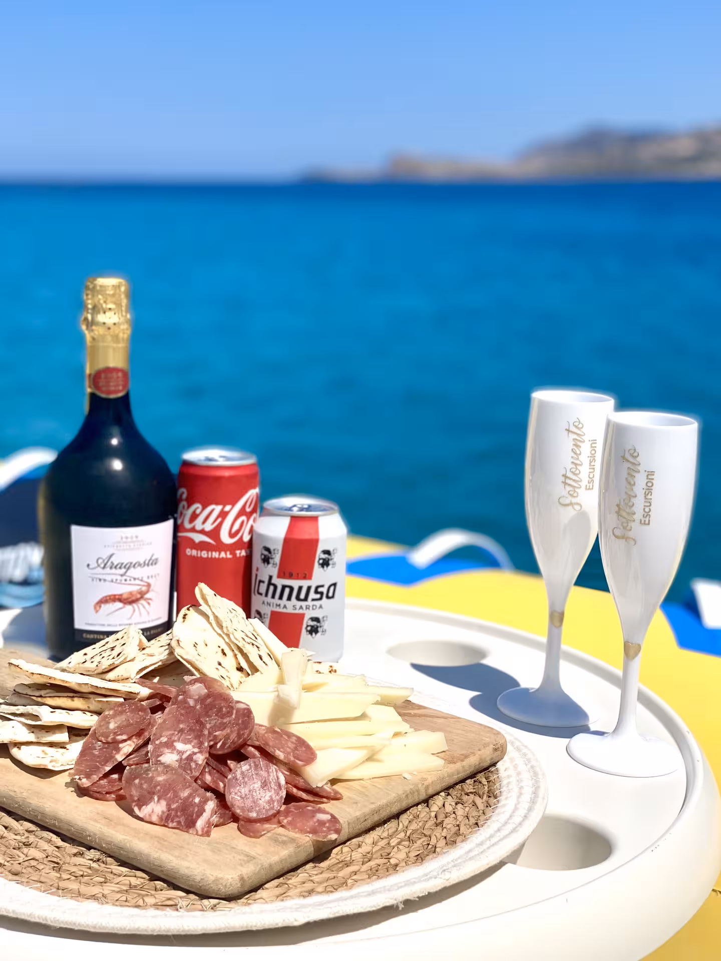 Gourmet aperitif setup on a dinghy with meats, cheese, and drinks, overlooking the stunning Asinara sea backdrop.