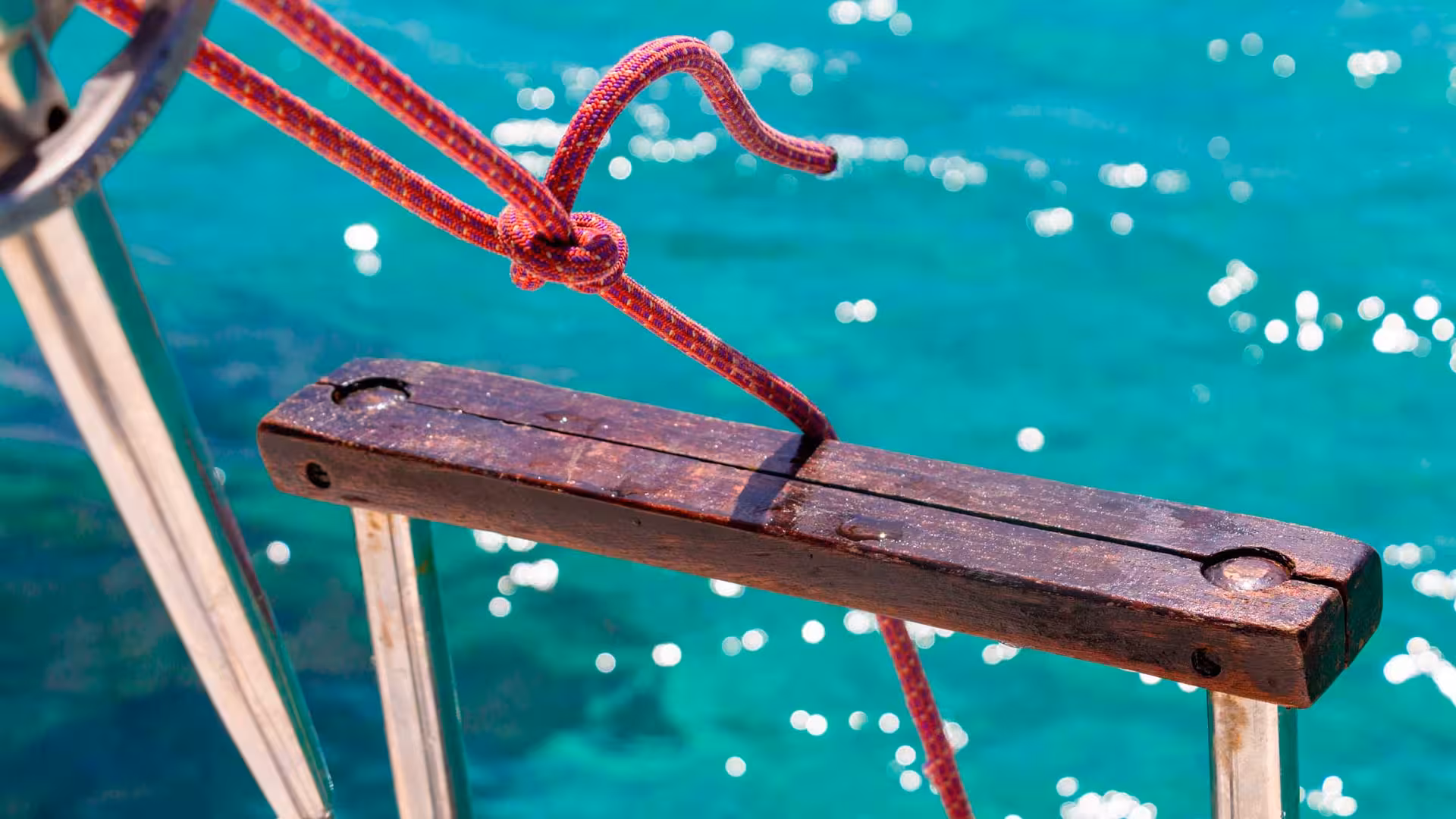 Red rope tied on a wooden cleat against the backdrop of clear turquoise water on the Asinara sailboat tour.