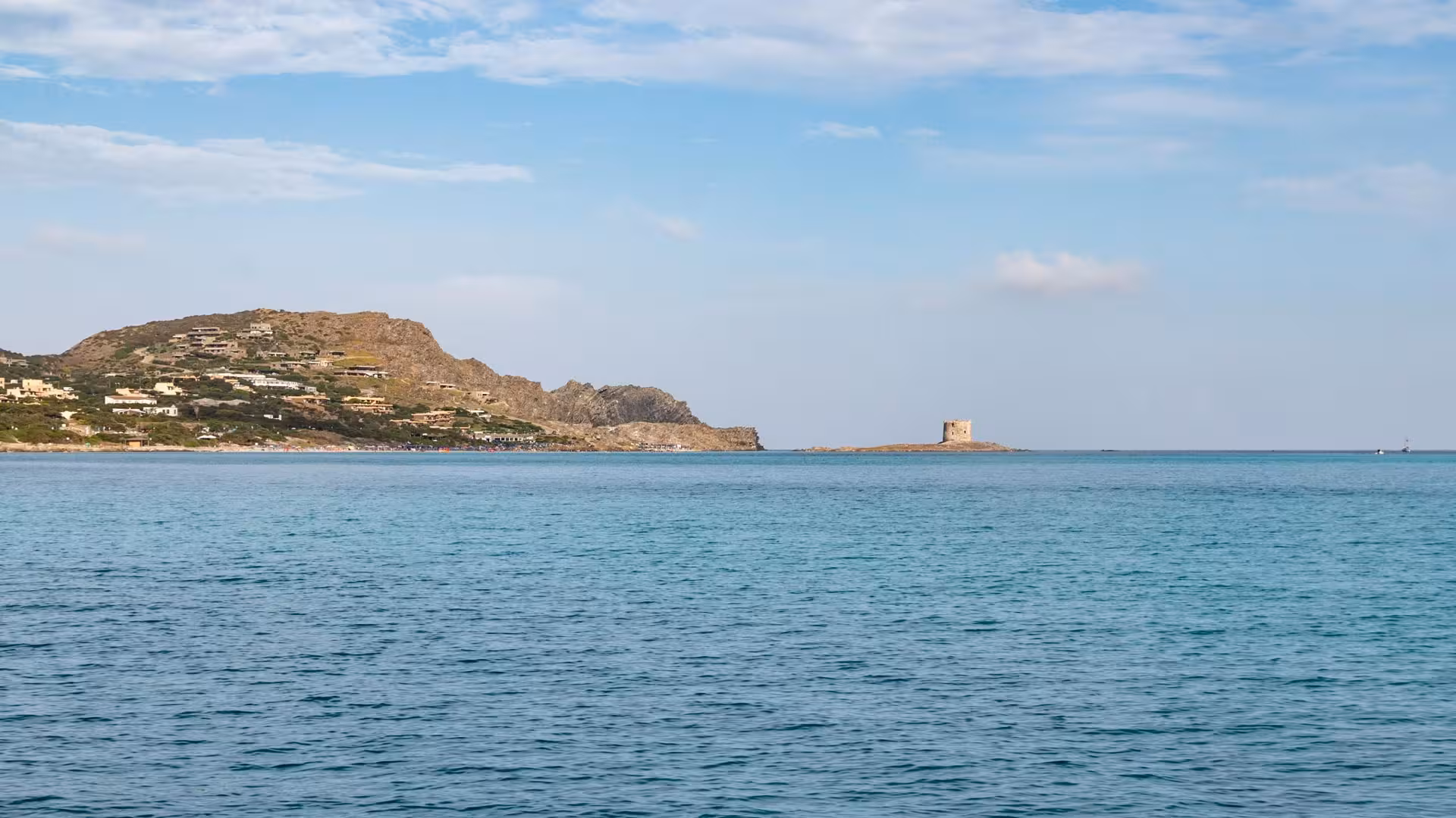 Scenic view of Asinara Island coastline from a catamaran, featuring clear blue waters and rocky landscapes.