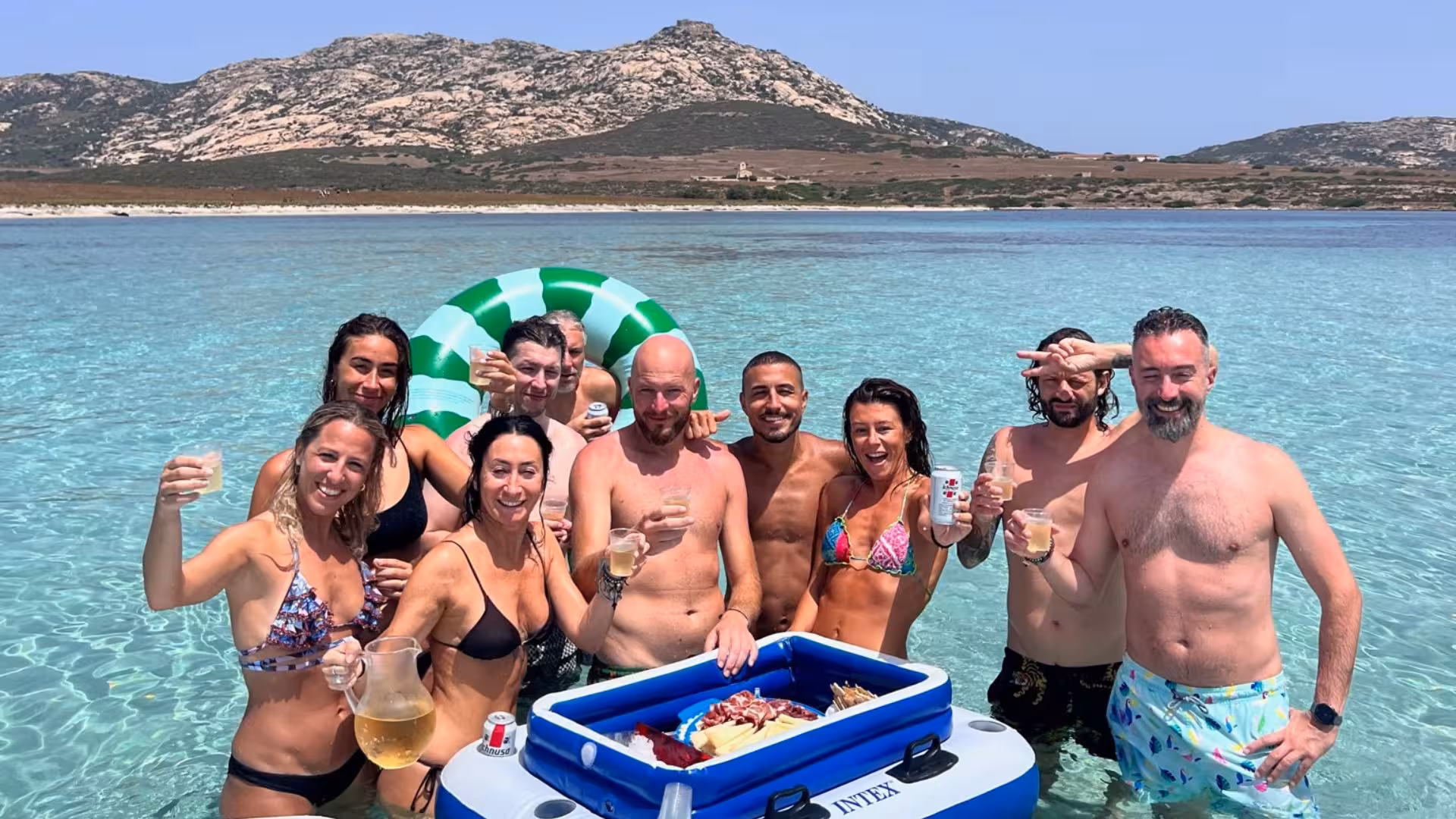 Group enjoying drinks and snacks in the clear waters of the Gulf of Asinara on a catamaran trip from Stintino.