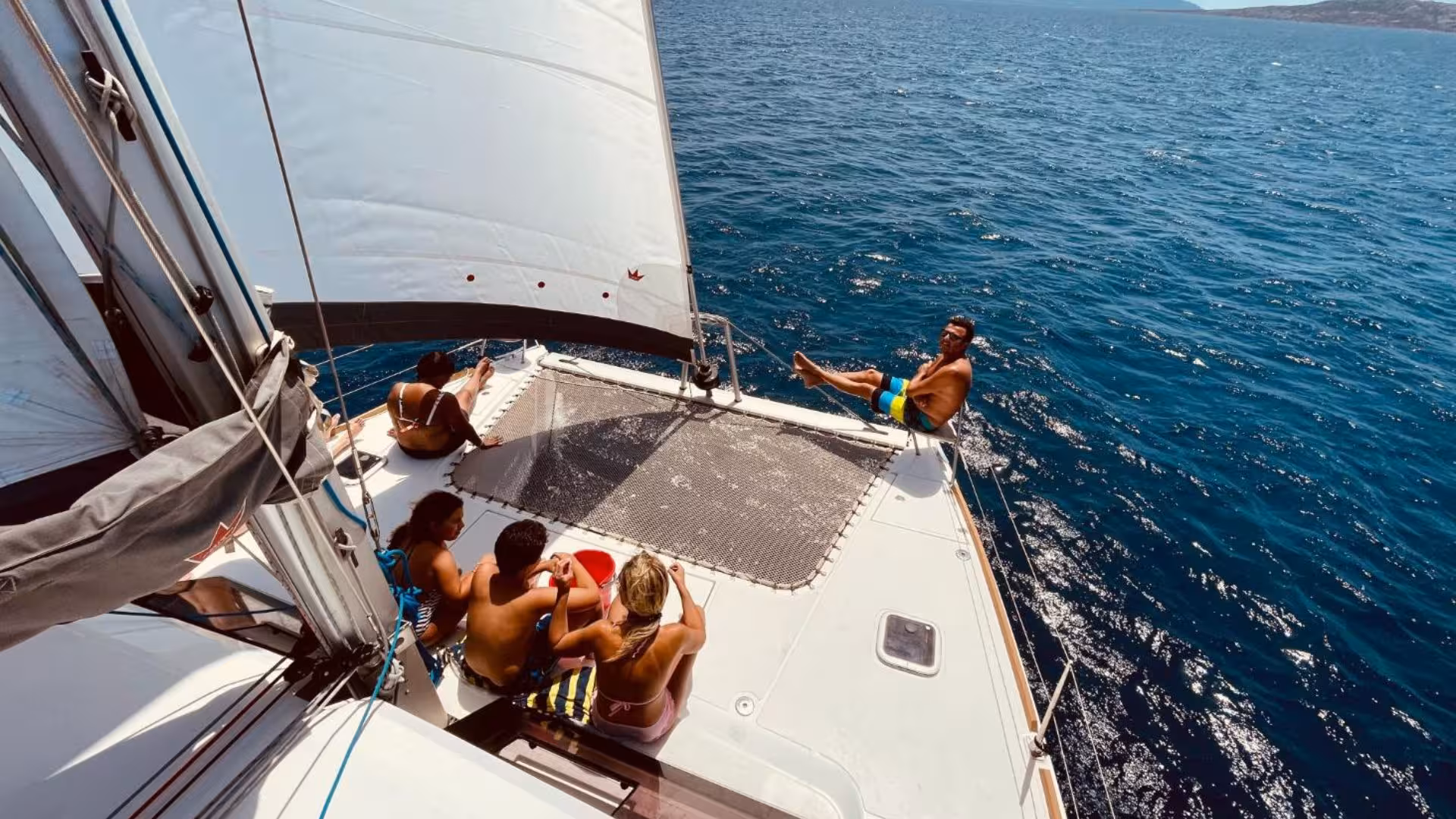 Group enjoying sunny day on catamaran deck during Stintino tour to La Pelosa with refreshing aperitif.