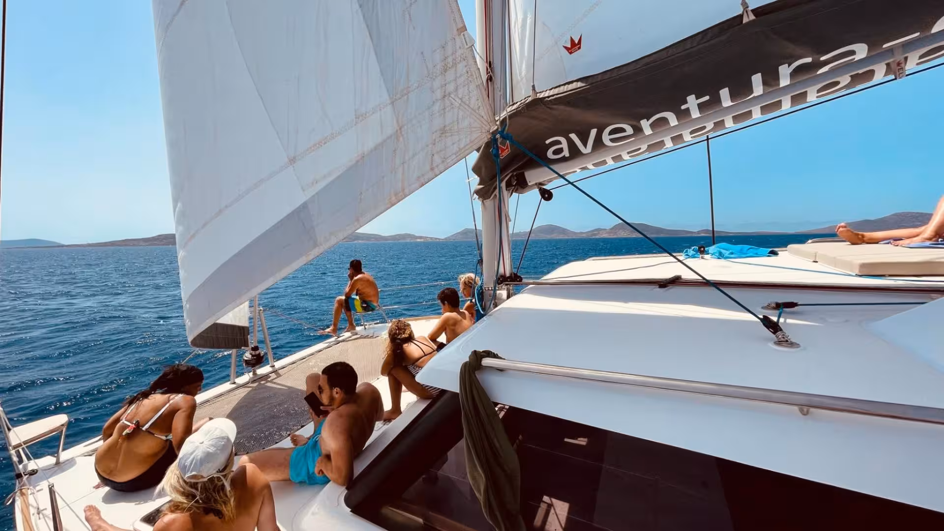 Relaxed passengers on a sailing catamaran headed towards La Pelosa's scenic views on a Stintino tour.