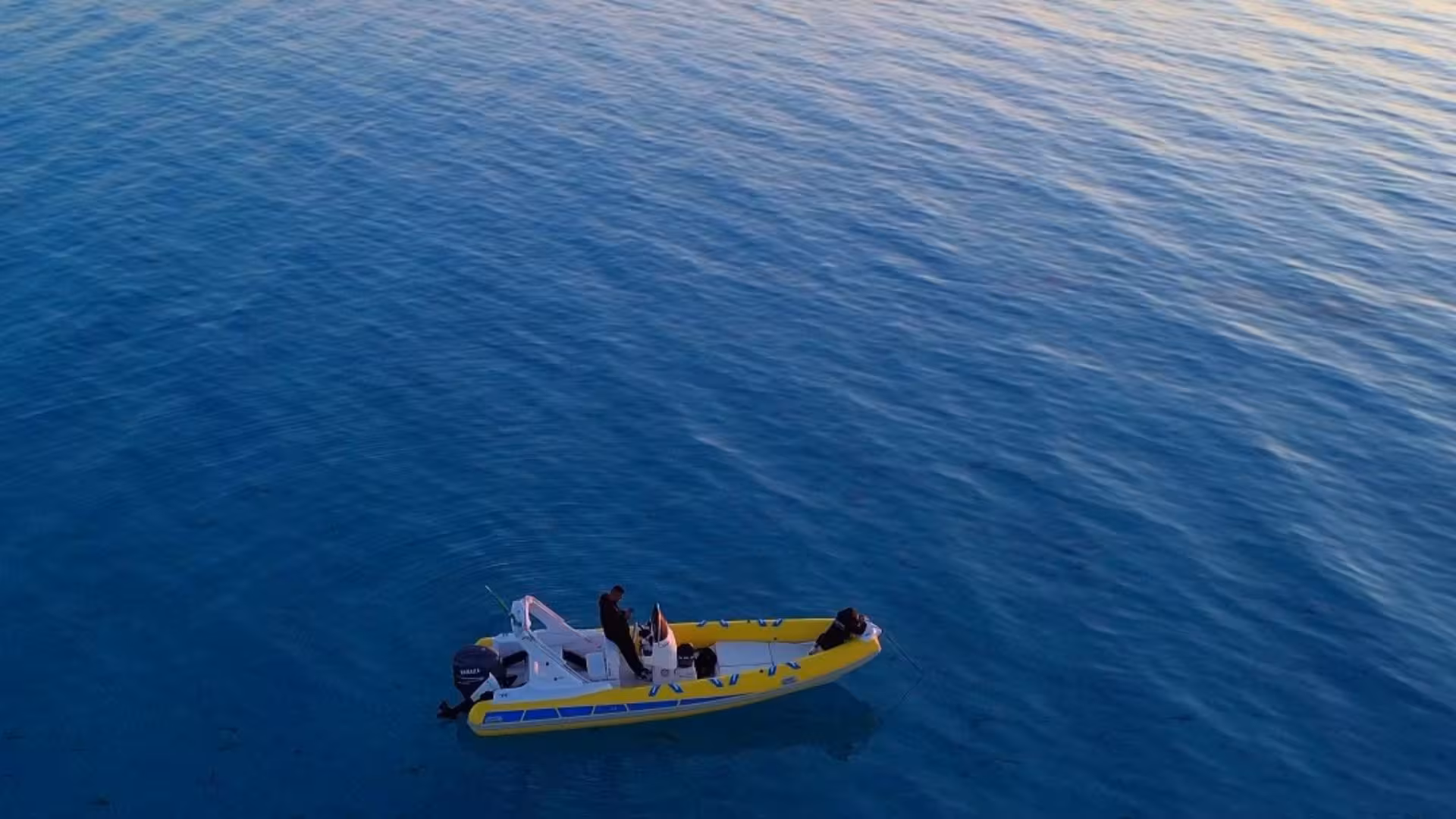 Aerial shot of a dinghy sailing on calm blue waters during a sunset tour from Stintino.