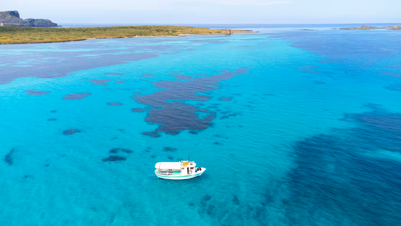 Scenic aerial view of a fishing boat on Asinara Park's crystal-clear waters, ideal for a Stintino boat tour.
