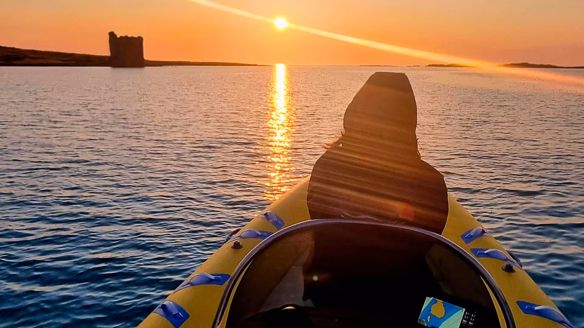 Person enjoying a sunrise dinghy tour near Stintino, with the sun reflecting on the water and a distant tower.