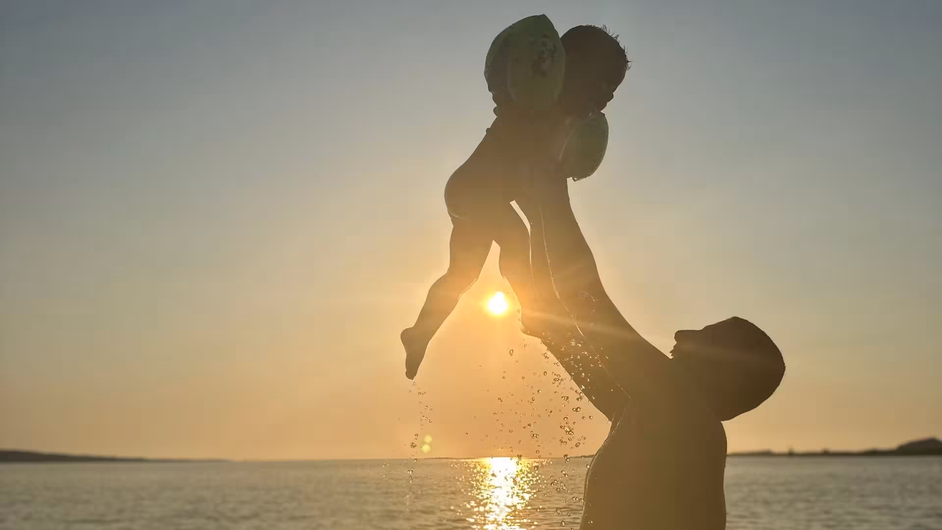 A joyful moment of a child being lifted against a stunning sunset during a Stintino catamaran tour in the Gulf of Asinara.