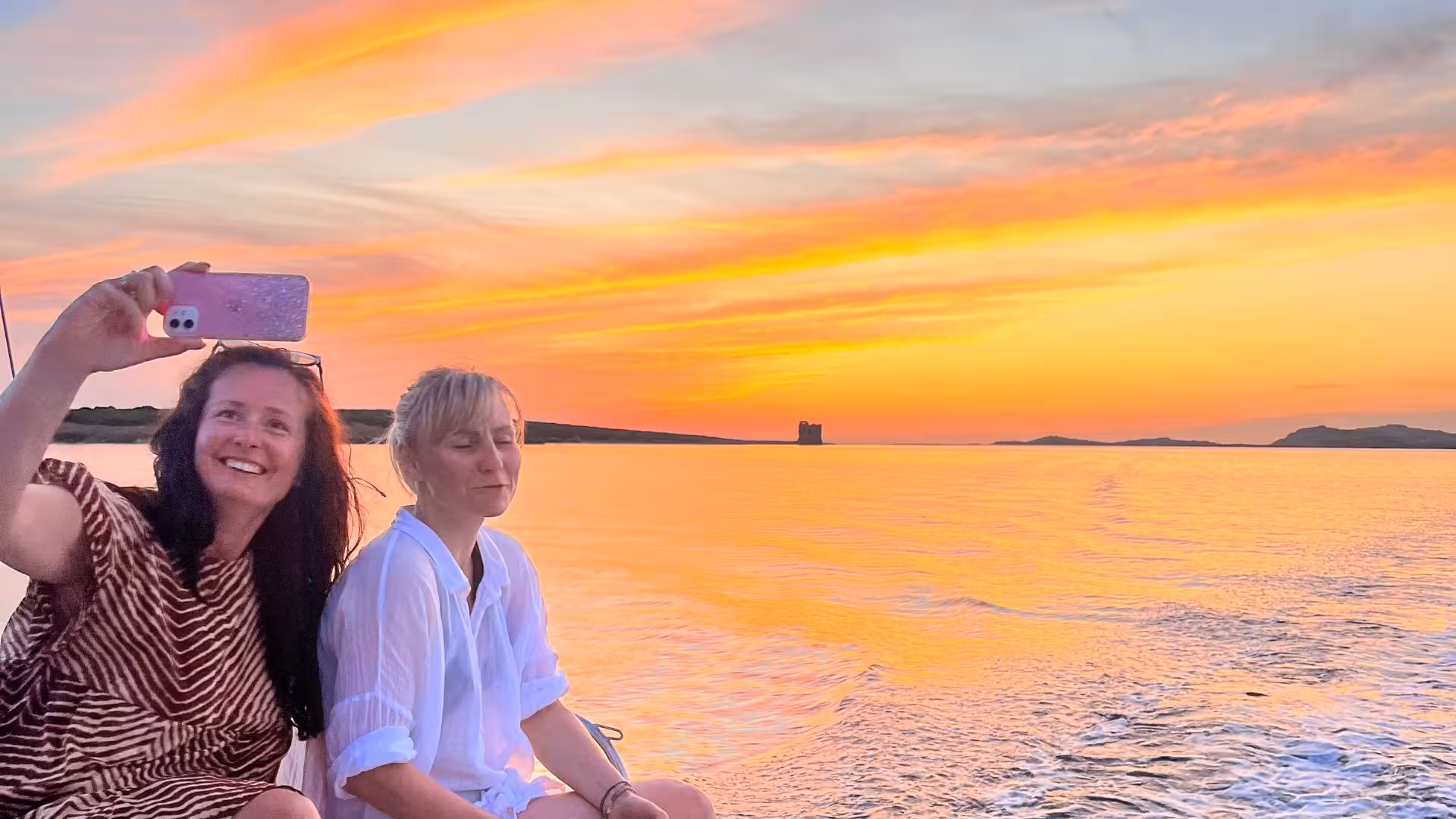 Two people capturing a vibrant sunset selfie on a catamaran tour in the Gulf of Asinara.